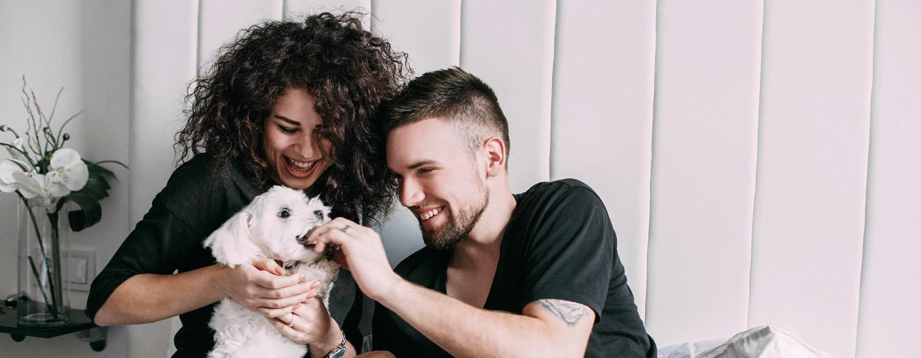 a man and woman sitting on a bed playing with a dog